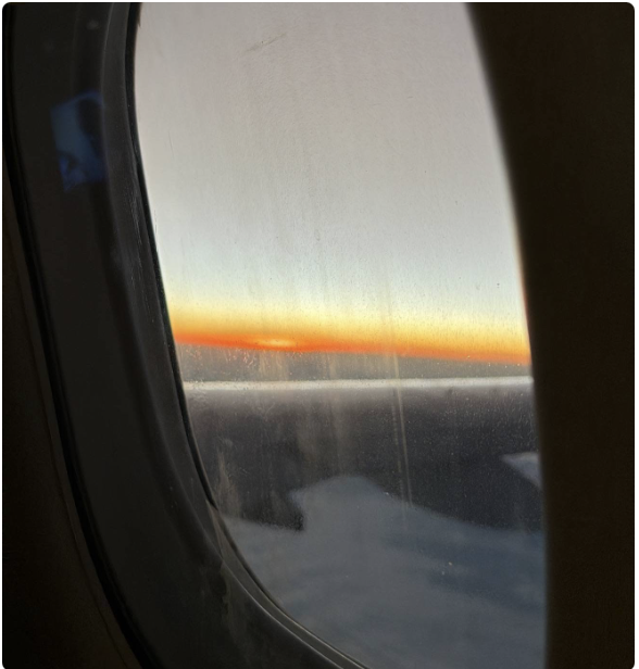 Janela de um avião, por do sol e nuvens.